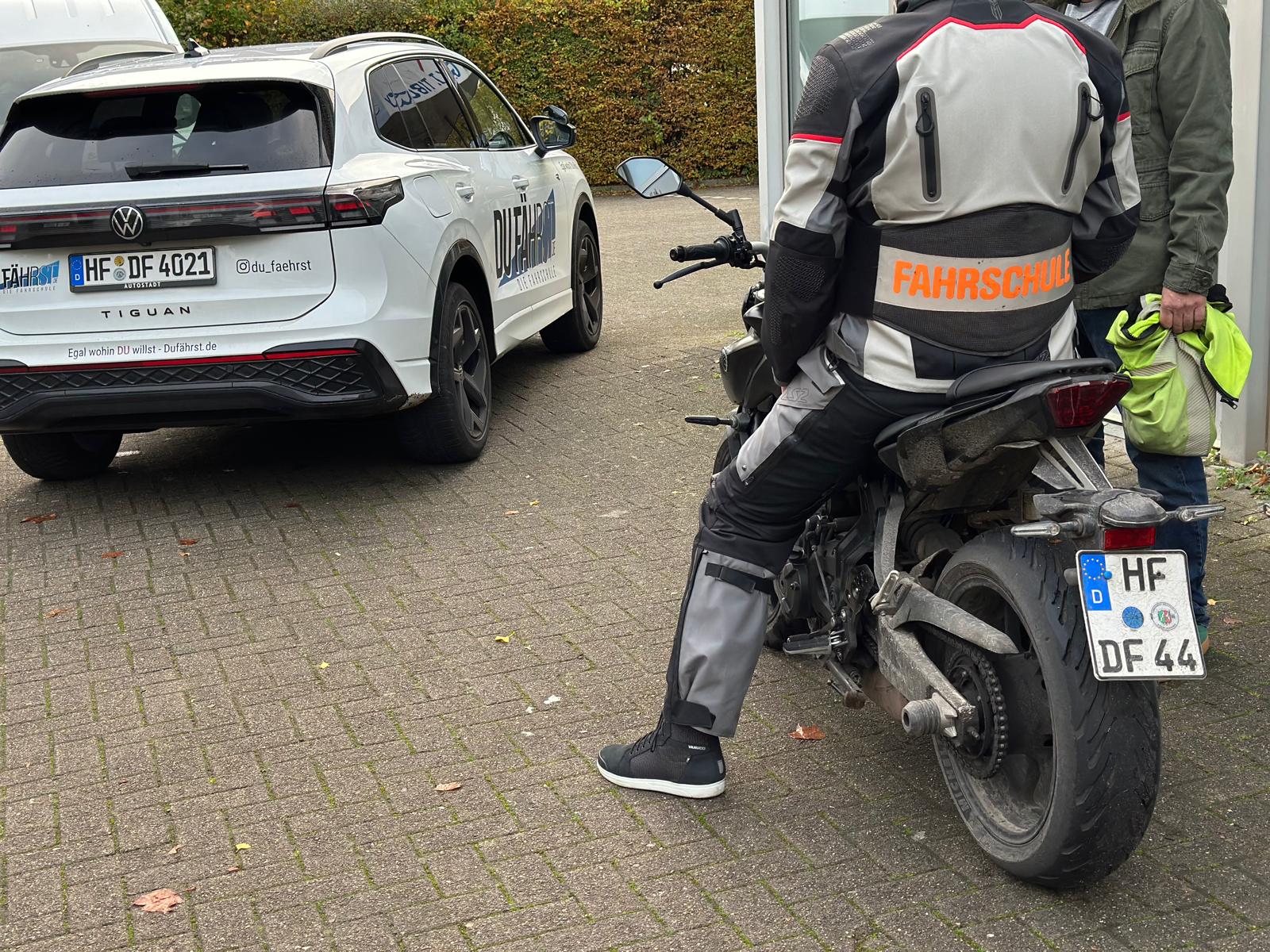 Einblick in die Motorrad-Ausbildung bei DU FÄHRST: Fahrschüler auf einem Motorrad neben einem Fahrschulwagen.